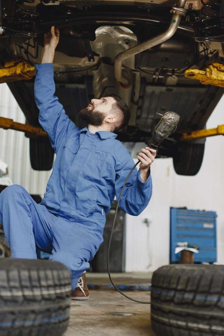 Mecánico revisando ruedas y frenos bajo el auto elevado